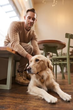 A dog friendly cafe concept. Handsome man, golden retriever owner sits in a cafe with his pet, drinks coffee and enjoys the day.