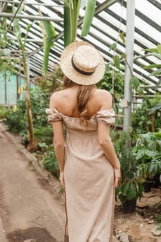 A beautiful young woman takes care of plants in a greenhouse. The view from the back. Concept of gardening and an eco-friendly lifestyle.