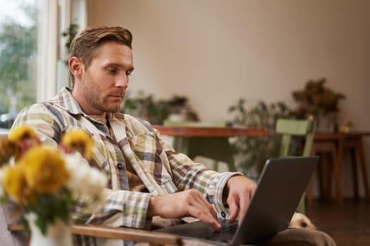 Lifestyle and workplace concept. Young handsome man in casual clothes, sitting in cafe with laptop, studying online, working remotely from coffee shop.