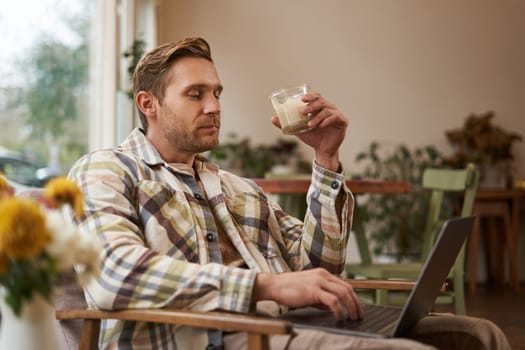 Handsome blond man with laptop, sitting in cafe and drinking coffee, working online, freelancing, set up workspace outside of an office environment.