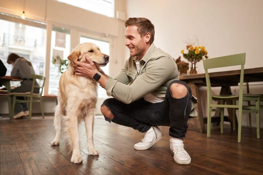 Close up portrait of happy dog owner, man with his pet giving a treat, spending time in animal-friendly cafe or co-working space.