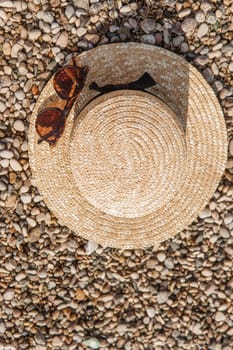 A straw hat and sunglasses on the beach. Pebbles on the seashore, close-up. The natural background