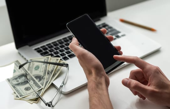 Mixed race man in glasses working with multiple electronic internet devices. Freelancer businessman has tablet and cellphone in hands and laptop on table with charts on screen. Multitasking theme. High quality photo