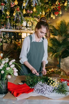 A woman in her florist shop collects bouquets of flowers. The concept of a small business. Bouquets of tulips for the holiday on March 8