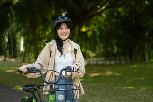 Smiling young woman in helmet walking with bicycle in city park on beautiful spring day.