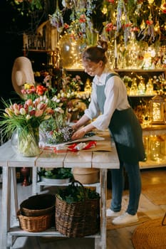 A woman in her florist shop collects bouquets of flowers. The concept of a small business. Bouquets of tulips for the holiday on March 8