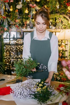 A woman in her florist shop collects bouquets of flowers. The concept of a small business. Bouquets of tulips for the holiday on March 8