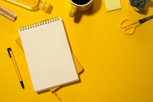 Blank spiral notepad, water bottle and stationery on yellow background with copy space.