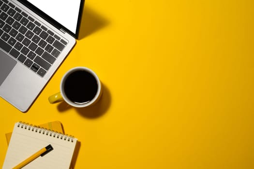 Laptop, cup of coffee and blank notepad on yellow background with copy space.