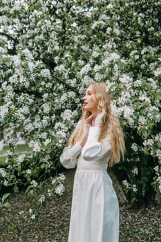 A blonde girl with long hair on a walk in a spring park. Springtime and blooming apple trees