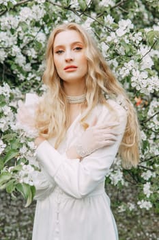 A blonde girl with long hair on a walk in a spring park. Springtime and blooming apple trees