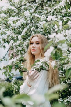 A blonde girl with long hair on a walk in a spring park. Springtime and blooming apple trees