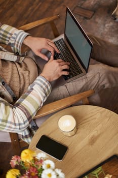 Vertical cropped portrait of man typing on laptop keyboard, freelancer working in cafe, using computer in coffee shop.