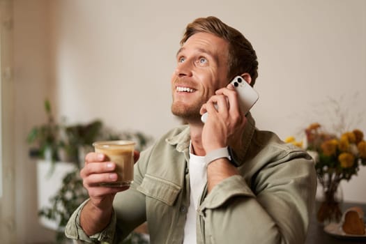 Portrait of handsome young man talking on the phone, sitting in cafe and drinking coffee, answering a call.