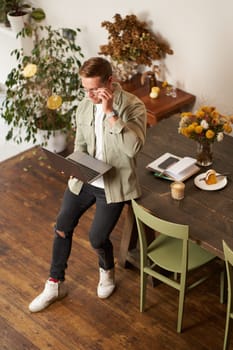 Portrait of handsome young man sits with laptop, looks at screen with concentrated, thoughtful face, working on a project, e-learning at co-working space, drinking coffee.