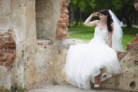 The brunette bride looks into the distance sitting on the ruins of an old fortress on a summer day