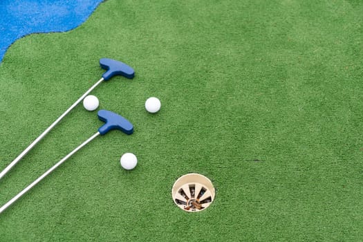 Mini-golf clubs and balls of different colors laid on artificial grass. High quality photo