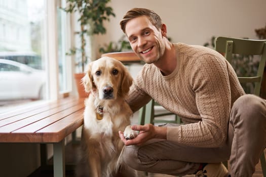 Portrait of a lovely golden retriever and handsome man in cafe. Cute dog gives paw and takes picture with his owner in coffee shop.