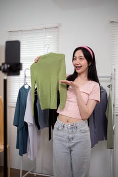 Woman asian online sell is using smartphone to while review shirt collection and talking with customer to selling online clothing on social media.
