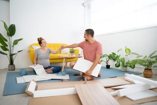 pregnant couple happily holding hands while assembling furniture in the new house. High quality photo