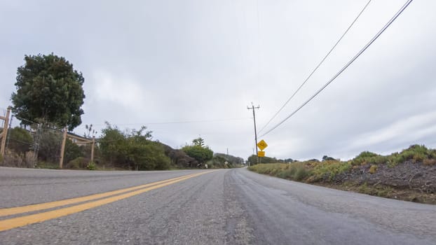 Vehicle navigates the streets of Morro Bay, California, during a cloudy winter day. The atmosphere is moody and serene as the overcast sky casts a soft light on the charming buildings and quiet streets of this coastal town.