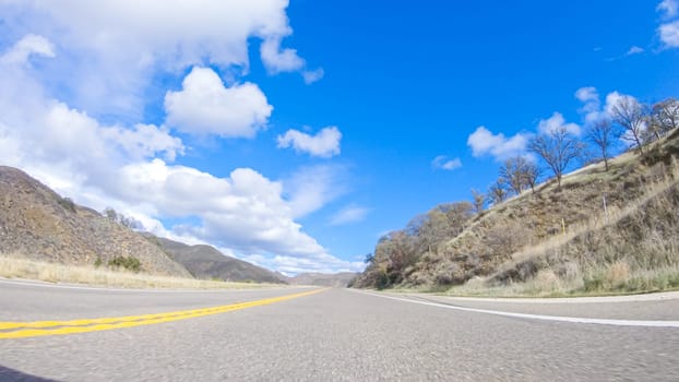 Vehicle is cruising along the Cuyama Highway under the bright sun. The surrounding landscape is illuminated by the radiant sunshine, creating a picturesque and inviting scene as the car travels through this captivating area.