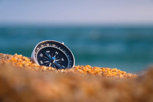 Conceptual photo of a compass in coarse sand against the background of the sea and sky, close-up, without people.