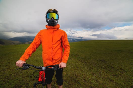Portrait of a racer in full protection of a full face mask on a bicycle or motorcycle in the summer mountains. The concept of attracting youth to outdoor sports.