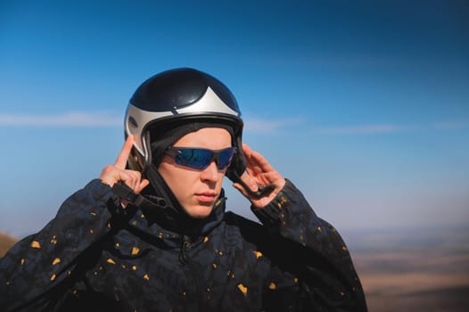A young male paraglider in sunglasses fastens his helmet on a sunny day. Preparing for paragliding.