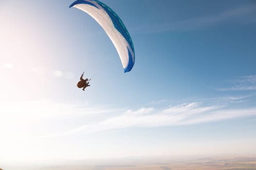 A paraglider with a blue parachute fly. A male flyght on the sky and lifts a paraglider into the air.