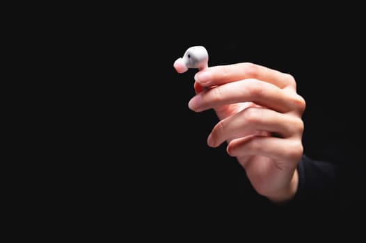 Close-up of a Caucasian girl's hand with an earphone on a black background. Demonstration of a modern wireless device.