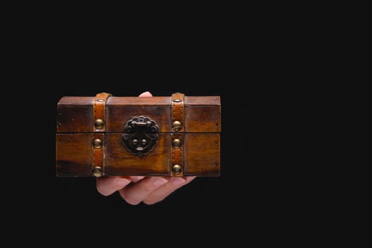 An old wooden box chest on a young female hand on a black background. Nice gift concept in gothic vintage style.