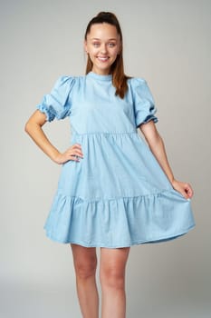 Young happy smiling woman in a light blue dress on a gray background close up