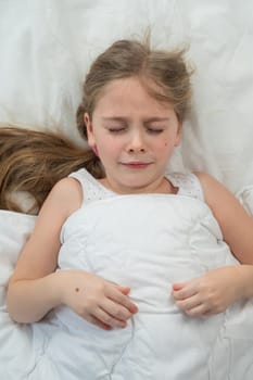 Top view of a little dissatisfied girl lying in bed. Vertical photo