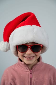 Portrait of a cute Caucasian girl wearing a Santa Claus hat and sunglasses on a white background