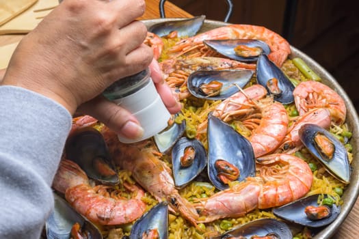 Close-up of a hand seasoning traditional seafood paella with rich colors, typical Spanish cuisine, Majorca, Balearic Islands, Spain,