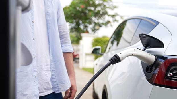 Modern eco-friendly man recharging electric vehicle from home EV charging station. EV car technology utilized for home resident to future environmental sustainability. Synchronos