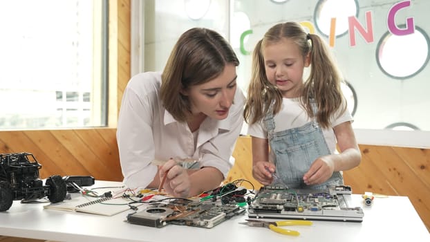 Young smart caucasian teacher teaching students about part of electronic board. Expert girl learn about digital electrical tool and fixing motherboard at table with chips and wires placed. Erudition.