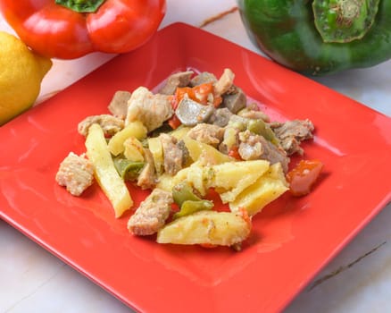 Pork with bell peppers and potatoes on a bright red plate, typical food, typical mediterranean mallorcan cuisine typical from balearic islands mallorca, spain,