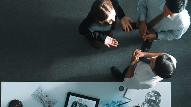 Top down view of smart engineer talking about turbine engine design while standing at meeting table with gear. Aerial view of technician discussing about electronic generator structure. Alimentation.