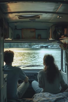 A man and a woman are sitting inside a motorhome and looking at the lake. Camping by the lake in a mobile home.