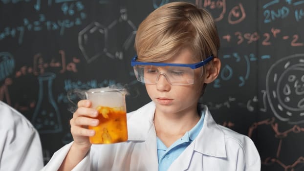 Smart boy inspect mixed chemical liquid in laboratory beakers while holding and looking carefully. Caucasian child focus on doing an experiment in chemistry lesson or STEM science class. Erudition.