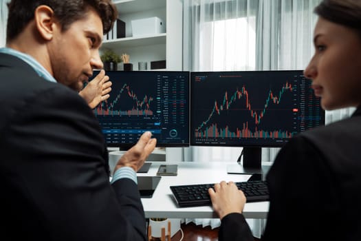 Two business traders discussing on dynamic stock market in currency rate investment trading on two pc screens with compare real time graph on risk or profit point of data at modern office. Postulate.