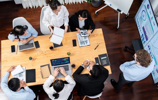 Wide top view of diverse group of business analyst team analyzing financial data report paper on meeting table. Chart and graph dashboard by business intelligence analysis. Meticulous