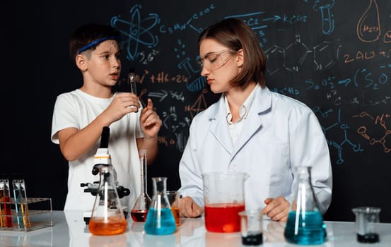 Teacher support schoolboy in laboratory. Schoolboy and teacher stand and experiment about science of chemistry in STEM class using liquid in glass container. Instructor mixing solution. Erudition.