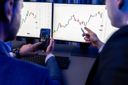 Two stock exchange traders researching data on smartphone and laptop screen server of dynamic digital currency. Investors analyzing market stock at decorative neon blue-light of workplace. Sellable.