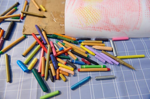 A background with scattered pastel color pencils on a table in the art class. View from above of many colorful crayons lying on the painter's desk. Visual art instruments. Drawing and painting tools