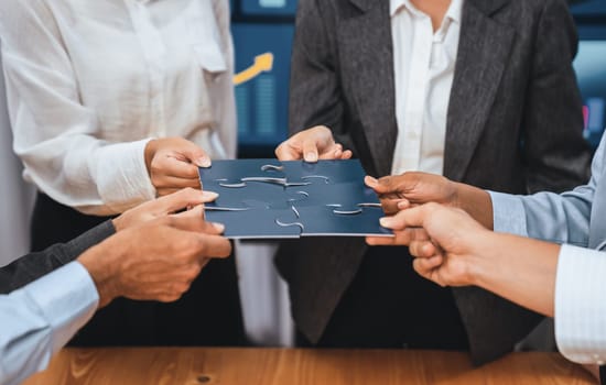 Corporate officer worker collaborate in office, connecting puzzle pieces with report paper on table as partnership and teamwork. Unity and synergy in business concept by merging jigsaw puzzle. Concord