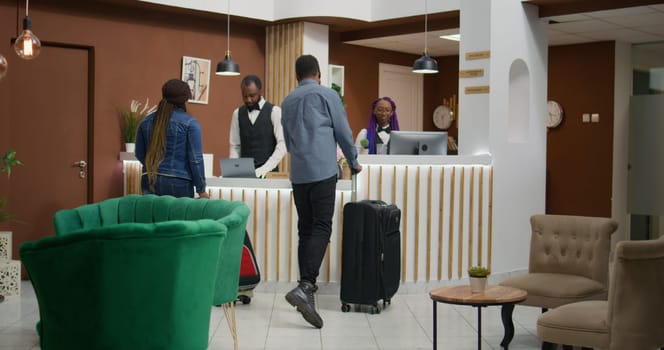 African american people arrive at hotel, talking to staff members about room booking and check in procedure. Man and woman arriving in lobby with trolley bags, honeymoon trip.
