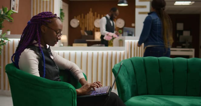 Staff member working on laptop in reception lobby, writing guest information on list to book room reservations. Woman concierge worker ensuring easy check in at luxurious hotel.